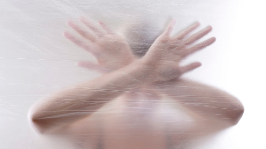 Person hinter Schleier mit gekreuzten Armen.