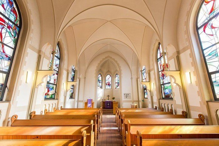 Kirchenschiff mit Bänken und Buntglasfenstern.