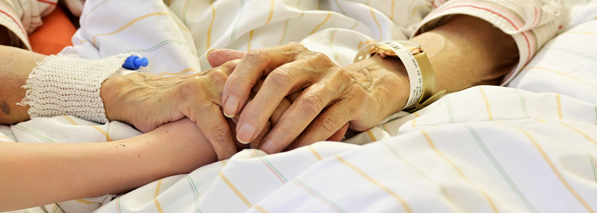 Hände halten sich im Krankenhausbett.